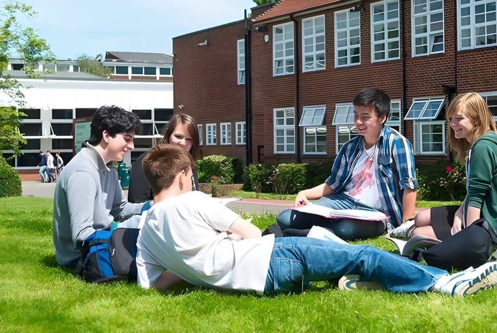 Schüler des Brockenhurst College sitzen auf der Wiese vor dem Backsteingebäude und lernen gemeinsam.