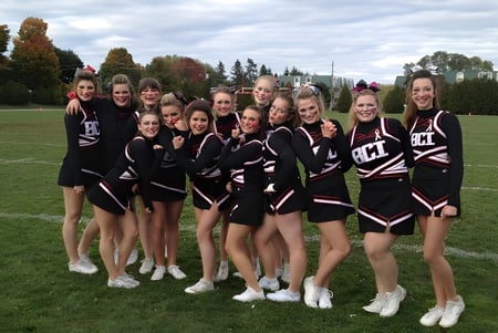 Eine Gruppe junger Cheerleaderinnen in schwarzen und weißen Uniformen steht auf dem Feld des Brockville Collegiate Institute.