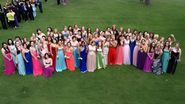 Eine große Gruppe Schülerinnen des Brockville Collegiate Institute in bunten Kleidern steht auf einer Wiese.