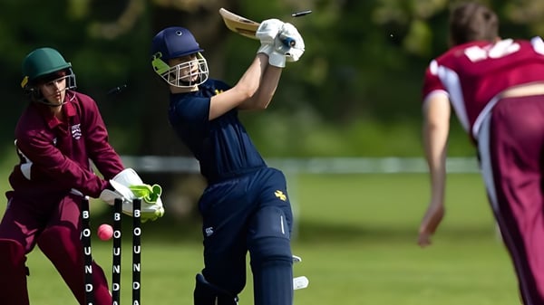 Ein Cricketspieler der Bromsgrove School schlägt den Ball auf einem grünen Spielfeld vor zwei weiteren Spielern.