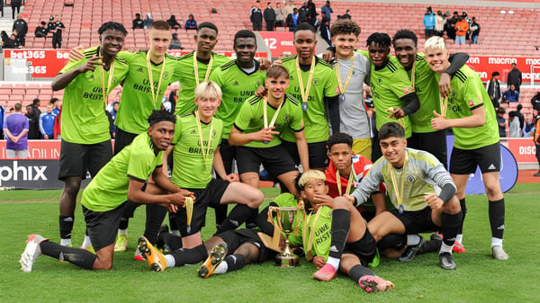 Eine Gruppe von Fußballspielern in grünen Trikots feiert zusammen auf dem Spielfeld des Brooke House College.