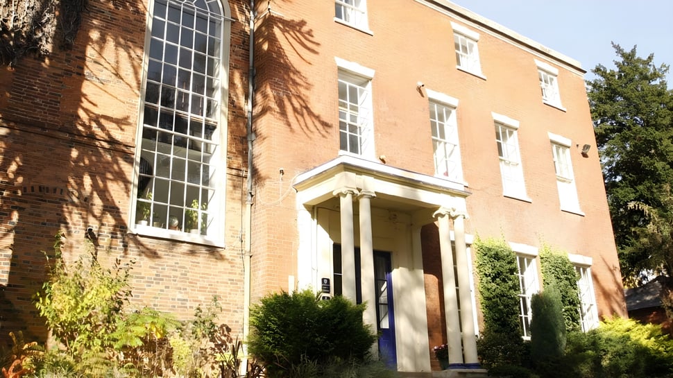 Das Backsteingebäude mit großen Fenstern und Eingang auf dem Campus der Brooke House College ist von Grünflächen umgeben.