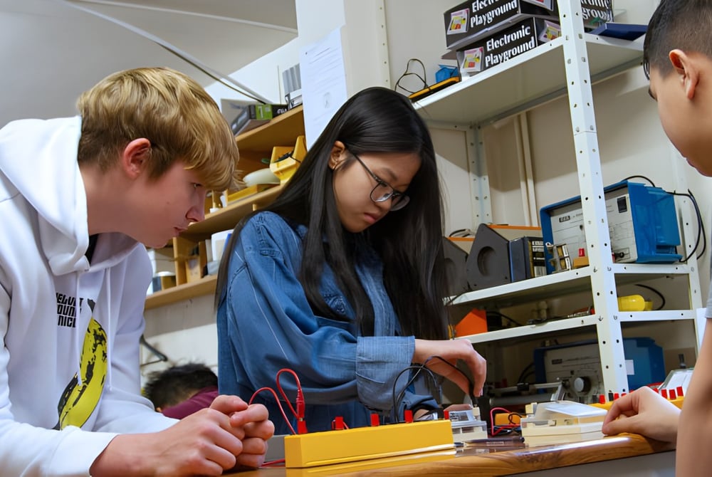 Drei Schülerinnen und Schüler der Brooke House College arbeiten gemeinsam an einem Projekt in einem Klassenraum.