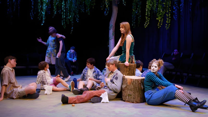 Eine Gruppe von Erwachsenen und Schülern sitzt und steht um einen Baumstumpf im Wald auf dem Gelände von Brooke House College.