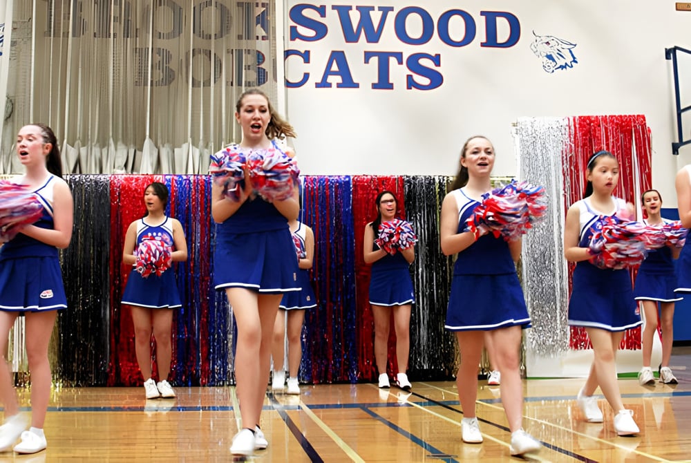 Schülerinnen und Schüler der Brookswood Secondary School führen Cheerleading auf einem Basketballfeld mit Swood Cats Schild im Hintergrund auf.