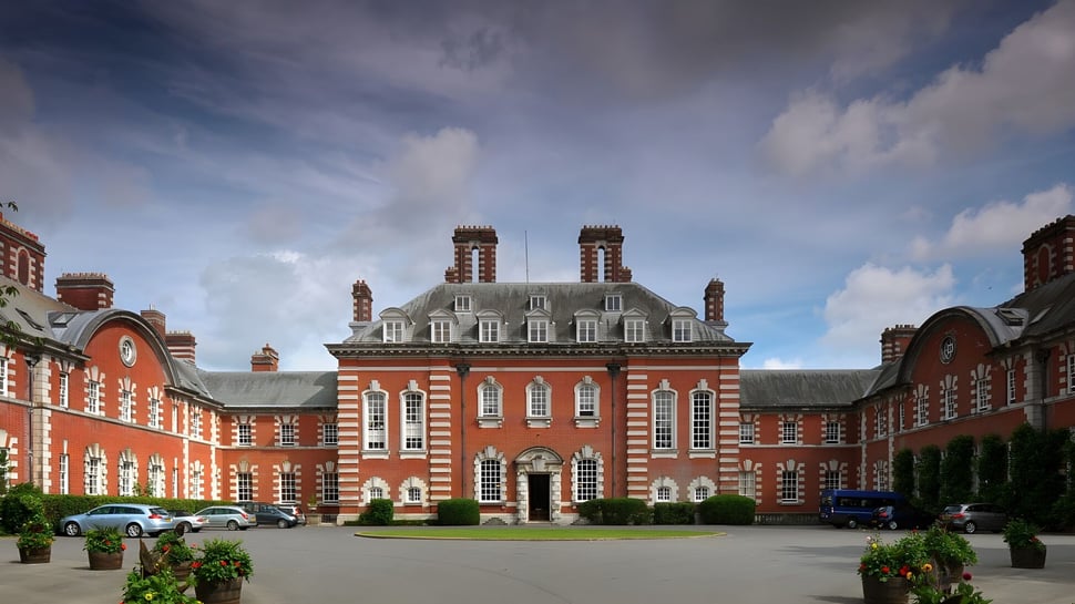 Das Hauptgebäude der Bryanston School steht in einem bepflanzten Innenhof mit umliegendem Grün und parkenden Autos.