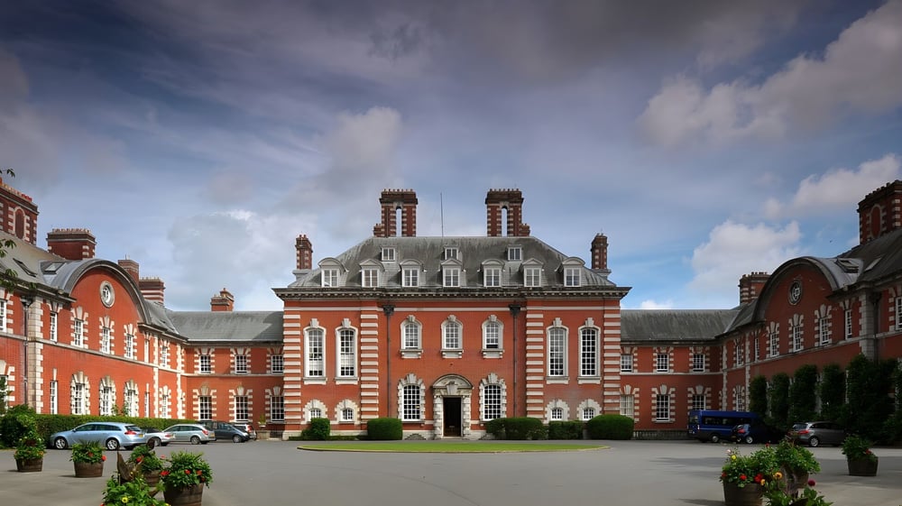 Das Hauptgebäude der Bryanston School steht in einem bepflanzten Innenhof mit umliegendem Grün und parkenden Autos.