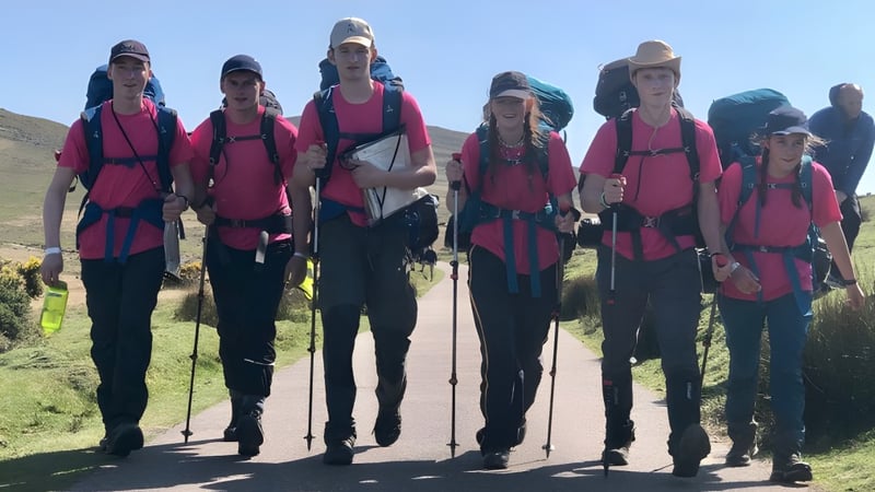 Eine Gruppe Schüler der Bryanston School steht in einheitlicher rosa Wanderausrüstung in einer landschaftlich reizvollen Umgebung mit Bergen im Hintergrund.