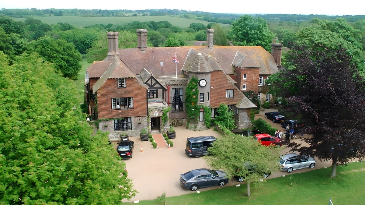 Ein Tudor-Herrenhaus umgeben von grüner Landschaft auf dem Gelände der Buckswood School mit parkenden Autos im Vordergrund.