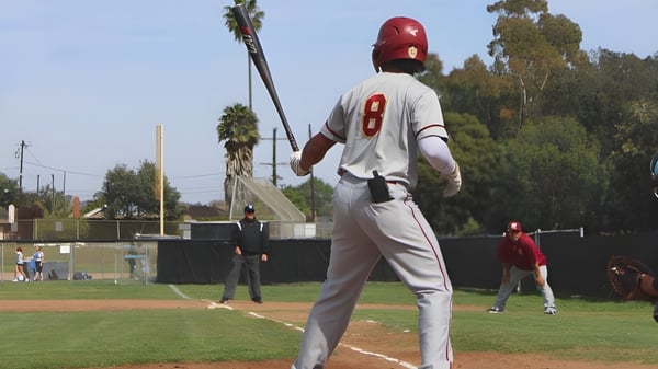 Ein Baseballspieler der Buena High School steht im weißen Trikot mit der Nummer 8 auf dem Spielfeld mit Palmen im Hintergrund.