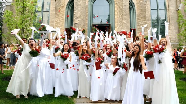 Schülerinnen und Schüler der Buffalo Seminary versammeln sich in weißen Roben mit roten Blumen vor einem verzierten Gebäude.
