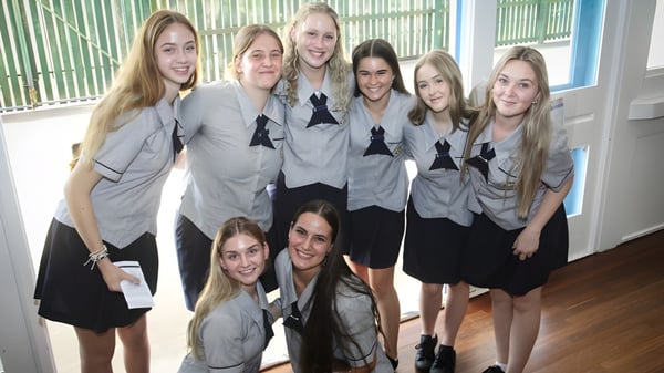 Eine Gruppe Schülerinnen der Bundaberg State High School steht gemeinsam in einem Raum mit grün-blauen gestreiften Wänden.