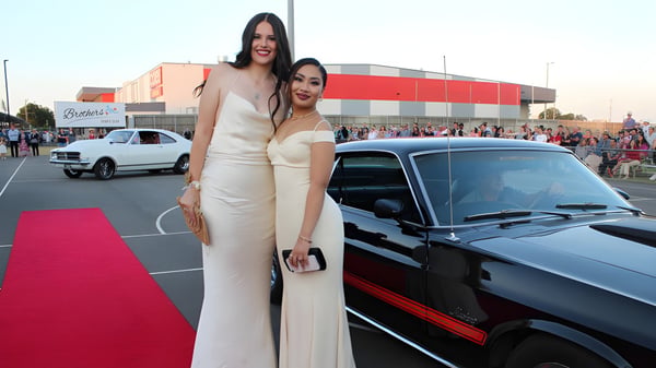 Zwei Frauen in eleganten Abendkleidern posieren auf dem roten Teppich vor einem Gebäude auf dem Campus der Bundaberg State High School.