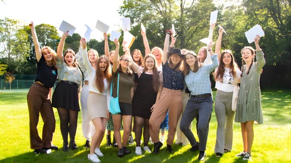 Eine Gruppe junger Schülerinnen der Burgess Hill Girls steht mit erhobenen Armen auf einer Wiese vor Bäumen im Freien.