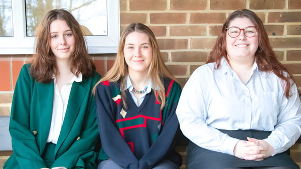 Drei Schülerinnen der Burgess Hill Girls stehen vor einer Backsteinwand.