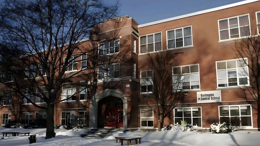 Das Backsteingebäude der Burlington Central High School steht vor schneebedeckten Bäumen unter klarem blauem Himmel.
