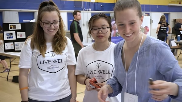 Drei Schülerinnen und Schüler mit Live Well T-Shirts stehen gemeinsam in einem Bildungsraum der Burlington Central High School.