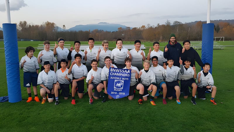 Eine Gruppe von Schülerinnen und Schülern der Burnaby Mountain School steht auf dem Fußballfeld mit Bergen im Hintergrund.