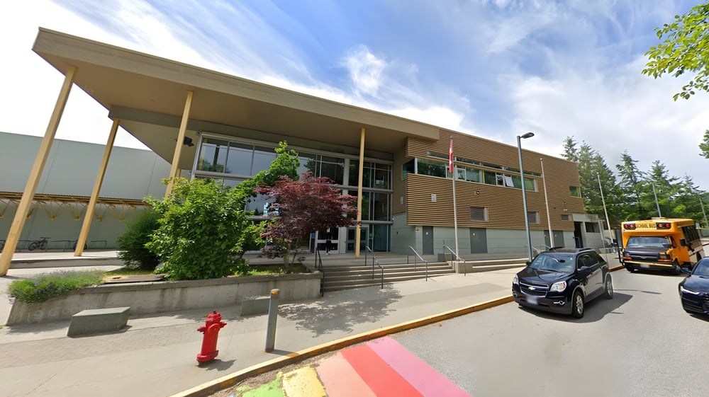 Das moderne mehrstöckige Gebäude der Burnaby Mountain School mit Glasfassade und überdachtem Eingang ist von Bäumen umgeben.