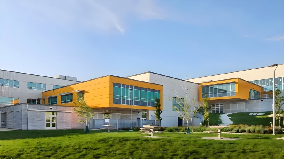 Das moderne mehrstöckige Gebäude der Burnaby North School mit gelber Fassade steht auf einem gepflegten Rasen umgeben von grüner Vegetation.