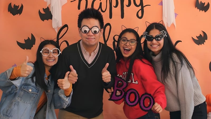 Eine Gruppe von vier Personen in Halloween-Kostümen vor einem orangefarbenen Hintergrund auf dem Campus der Burnaby North School.