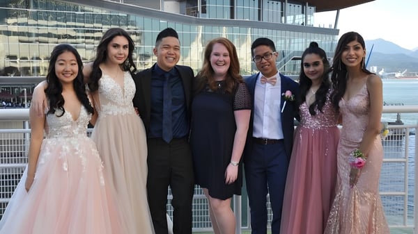 Eine Gruppe von Schülerinnen und Schülern in formeller Kleidung steht vor dem modernen Glasgebäude der Burnaby South School.