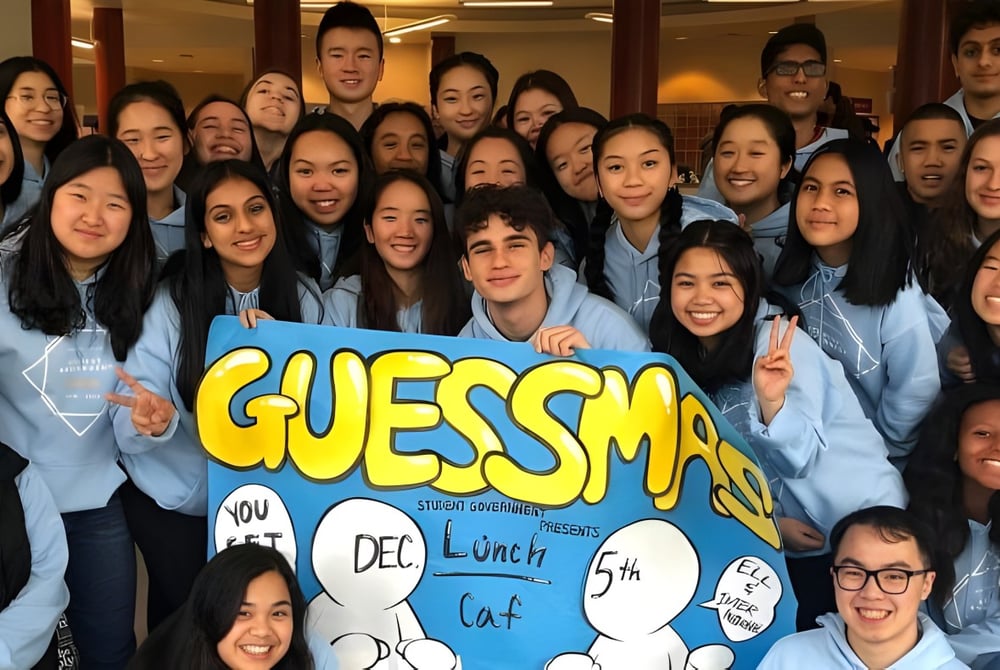 Schüler der Burnaby South School halten in einem hellen Innenraum ein großes Banner mit der Aufschrift GUESSMAS.