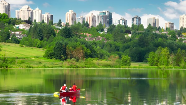 Zwei Personen paddeln in einem Kajak auf einem See vor der Kulisse moderner Gebäude auf dem Gelände der Burnaby South School.