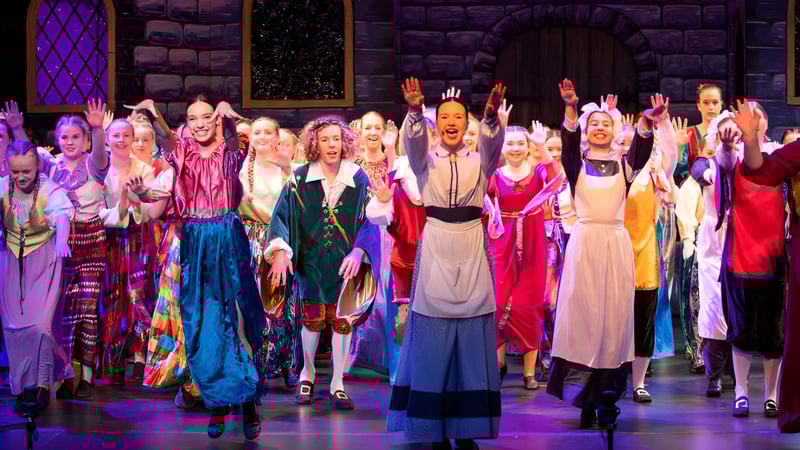 Schüler der Burnie High School stehen in bunten Kostümen auf der Bühne vor mittelalterlichem Steinhintergrund.