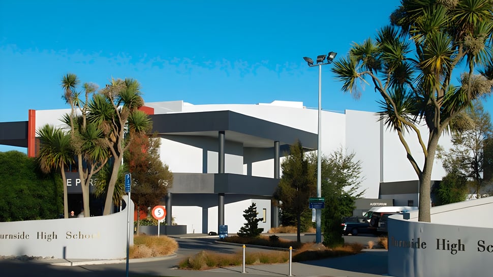 Das moderne mehrstöckige Schulgebäude der Burnside High School mit Palmen vor klarem blauen Himmel.