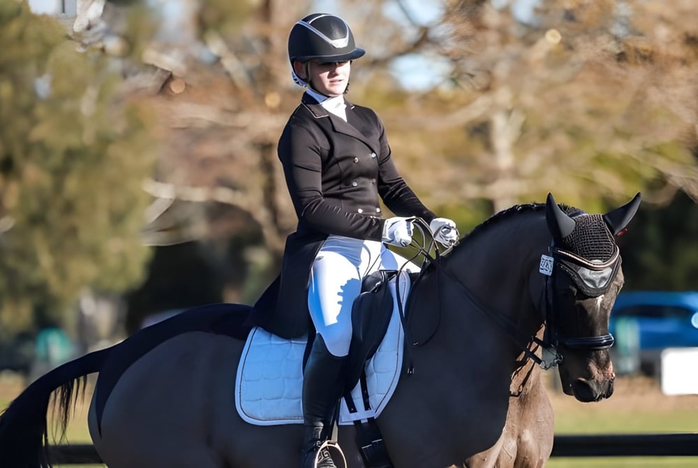 Eine Schülerin der Burnside High School reitet ein schwarzes Pferd im Freien mit Bäumen im Hintergrund.