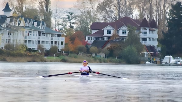 Eine Schülerin rudert auf dem Wasser mit herbstlicher Landschaft und Häusern im Hintergrund auf dem Gelände der Burnsview Secondary School.