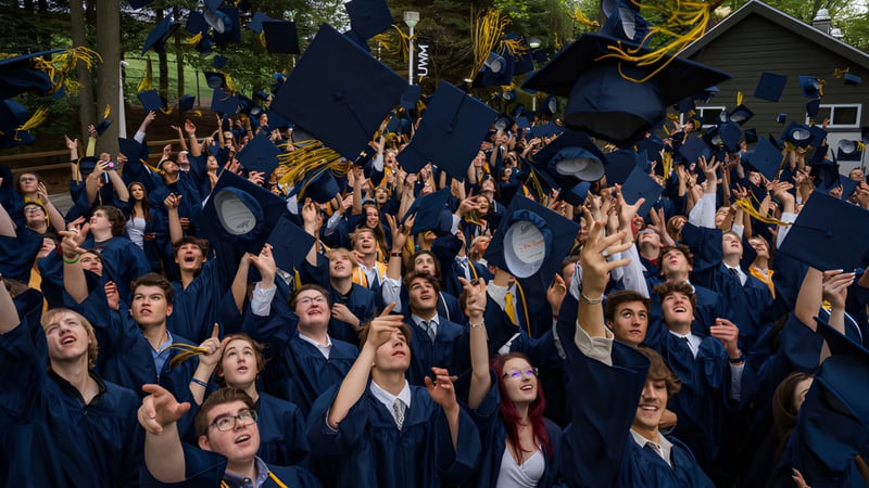 Absolventen der Burpengary State Secondary College feiern im Freien ihre Abschlussfeier in schwarzen Talaren und Hüten.