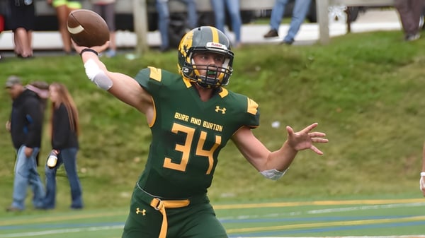 Ein Footballspieler der Burr and Burton Academy in grünem Trikot wirft einen Football auf dem Spielfeld.
