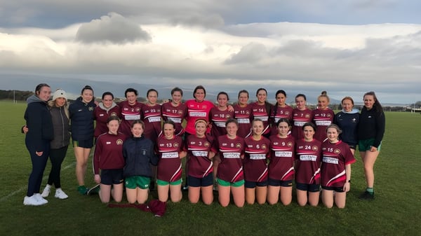Eine Gruppe junger Schülerinnen der Bush Post Primary School posiert auf einem grasbewachsenen Feld mit hügeliger Landschaft im Hintergrund.