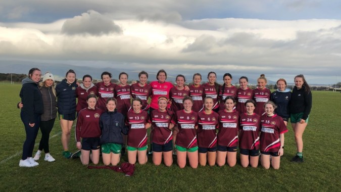 Eine Gruppe junger Athletinnen der Bush Post Primary School posiert gemeinsam auf einem Sportfeld mit Hügeln und bewölktem Himmel im Hintergrund.