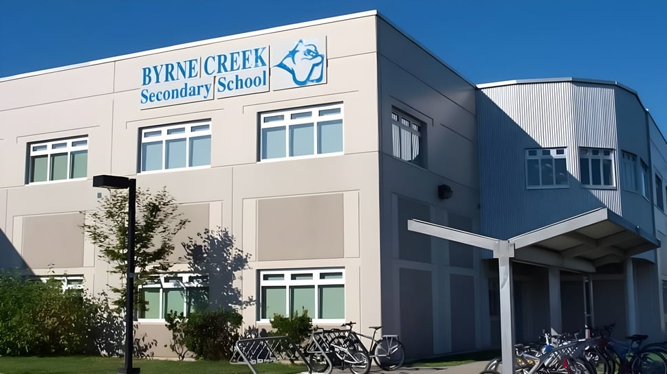 Das mehrstöckige Schulgebäude der Byrne Creek School ist von Bäumen umgeben und Fahrräder stehen davor.