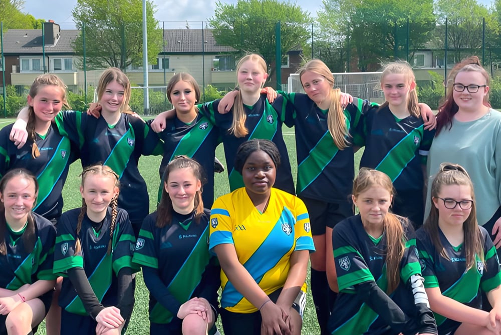 Eine Gruppe weiblicher Fußballspielerinnen posiert auf dem Sportplatz der Cabinteely Community School.
