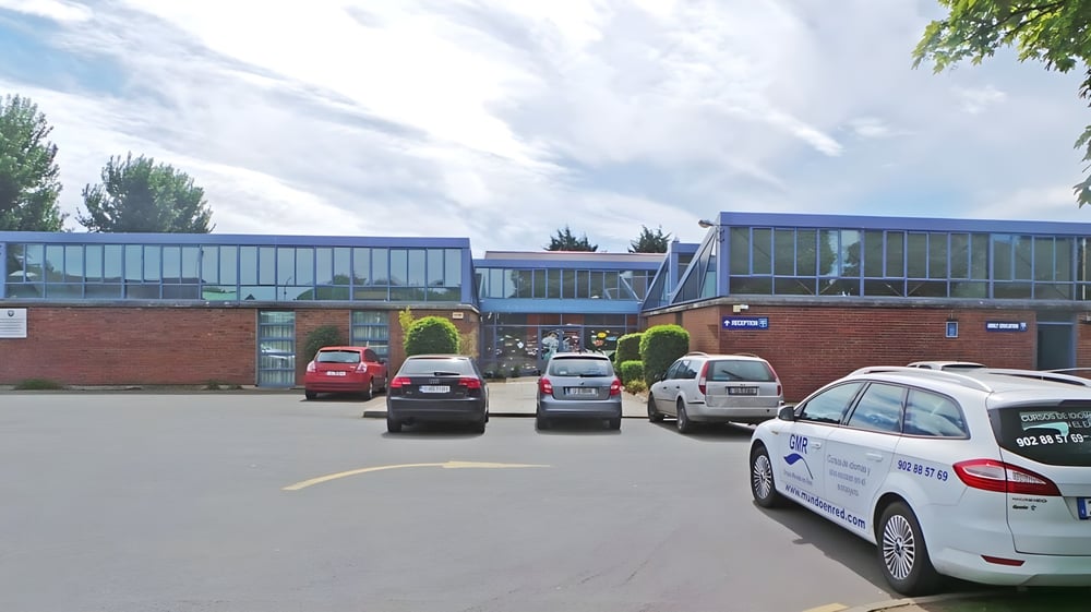 Der Parkplatz der Cabinteely Community School ist von Backsteingebäuden mit Glasfenstern umgeben, unter einem bewölkten Himmel.