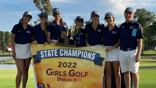 Eine Gruppe von Schülerinnen der Cactus Shadows High School hält eine Trophäe vor einem Banner der State Champions 2022 im Mädchen-Golf.