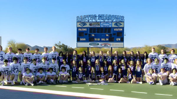 Fußballspielerinnen und Fußballspieler der Cactus Shadows High School stehen auf dem Spielfeld vor einer Anzeigetafel mit Bergen im Hintergrund.