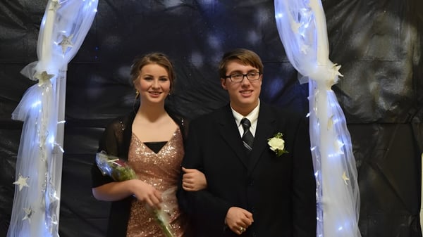 Ein formell gekleidetes Paar steht unter einem dekorativen Bogen bei einer Hochzeitsfeier auf dem Gelände der Cadillac Heritage Christian School.