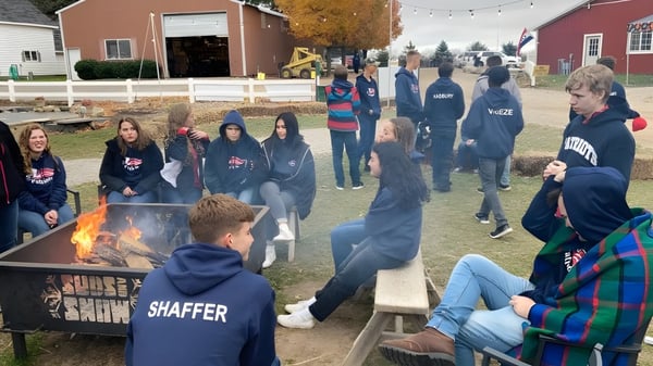 Schüler der Cadillac Heritage Christian School versammeln sich im Herbst draußen um eine Feuerstelle mit buntem Laub im Hintergrund.