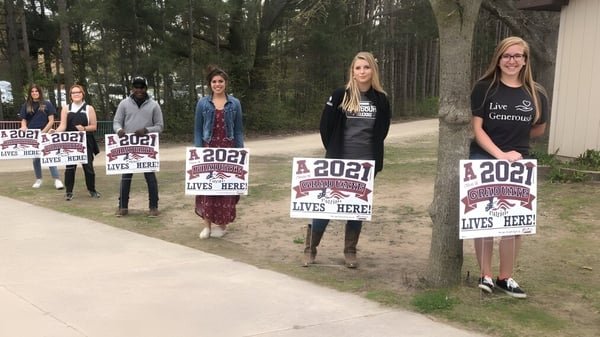 Eine Gruppe von Schülern der Cadillac Heritage Christian School steht mit Schildern auf einem Waldweg.
