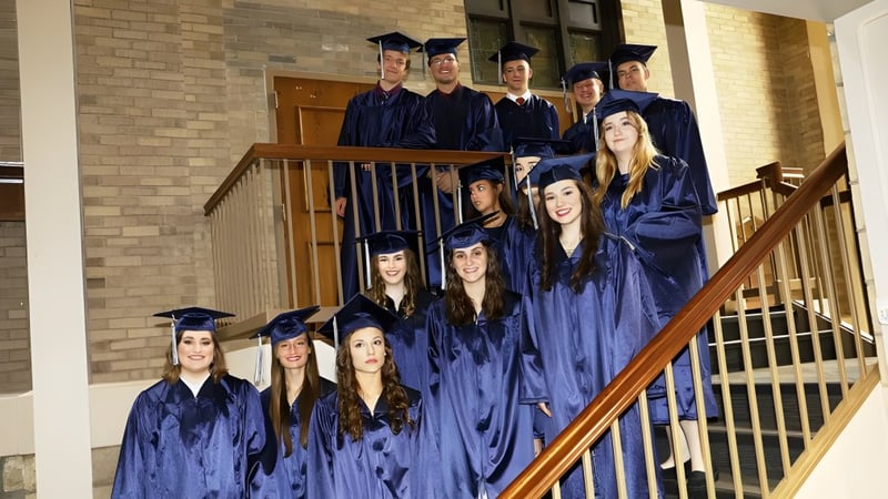 Eine Gruppe von Absolventen der Cair Paravel Latin School steht in blauen Talaren auf einer Treppe vor einem Backsteingebäude.