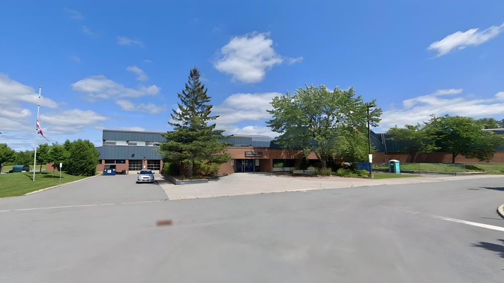 Das moderne mehrstöckige Gebäude der Cairine Wilson Secondary School mit großem Parkplatz und umgeben von Bäumen unter blauem Himmel.