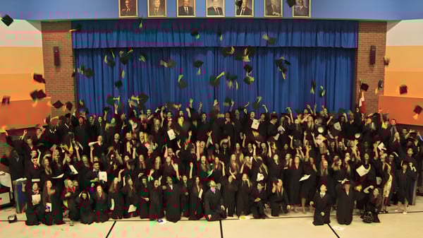 Absolventinnen und Absolventen der Cairine Wilson Secondary School feiern ihren Abschluss vor einer Bühne mit blauen Vorhängen.