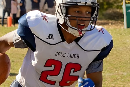 Ein junger Footballspieler der Cair Paravel Latin School steht mit Helm und Ball auf dem Spielfeld.