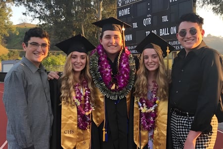 Eine Gruppe von Absolventen steht in akademischer Kleidung vor einem Logo auf dem Campus der Calabasas High School.