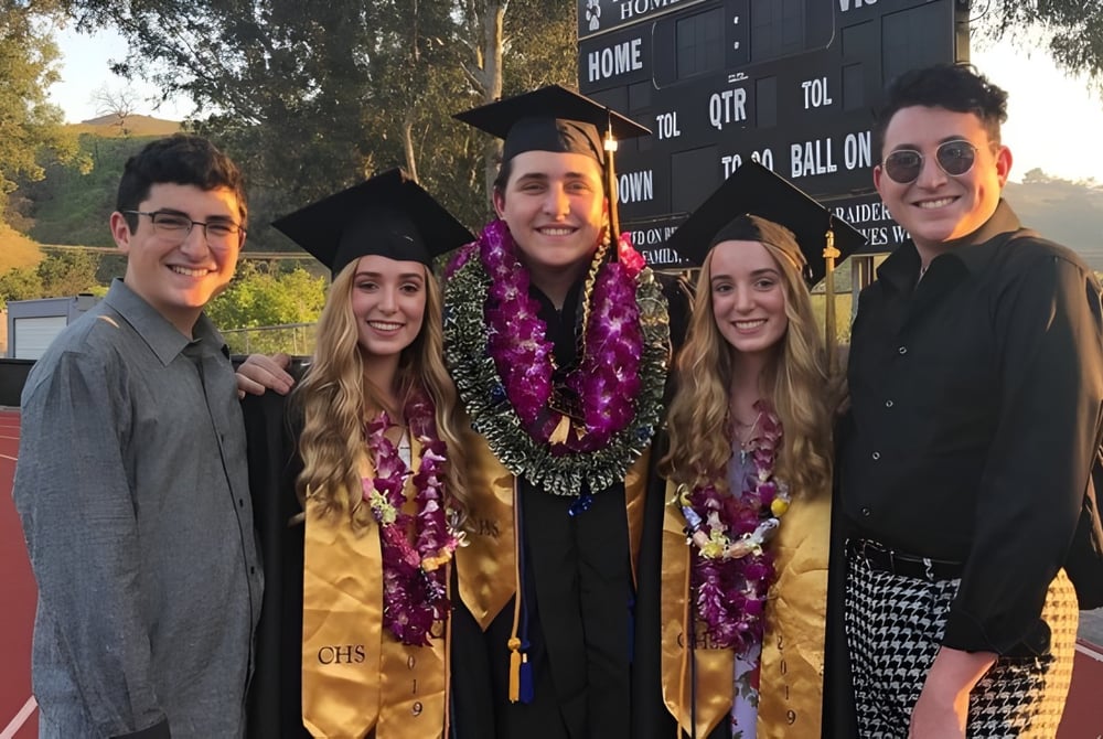 Eine Gruppe von Absolventen steht in akademischer Kleidung vor einem Logo auf dem Campus der Calabasas High School.